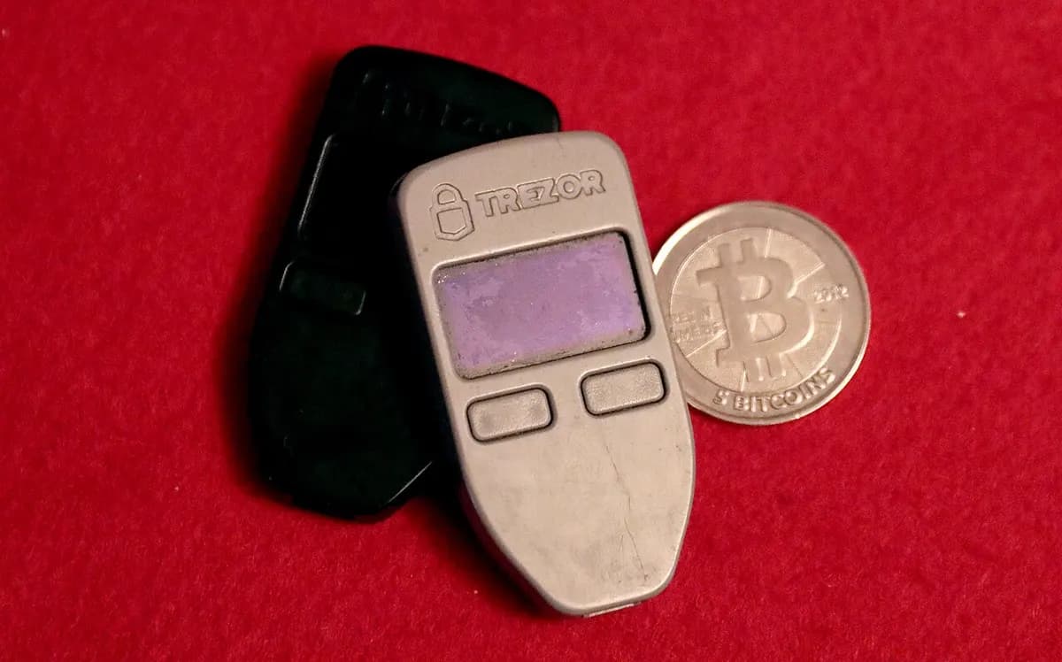 两台带屏幕的小型 Trezor One 硬件钱包，旁边是一枚实物 Casascius 比特币硬币。